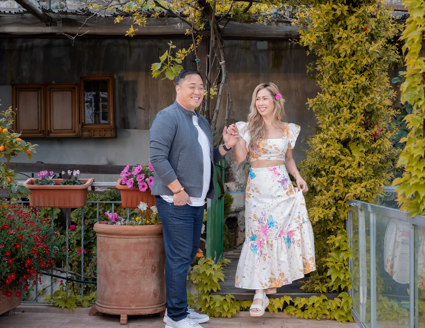 The couple standing outside the villa among flowering plants