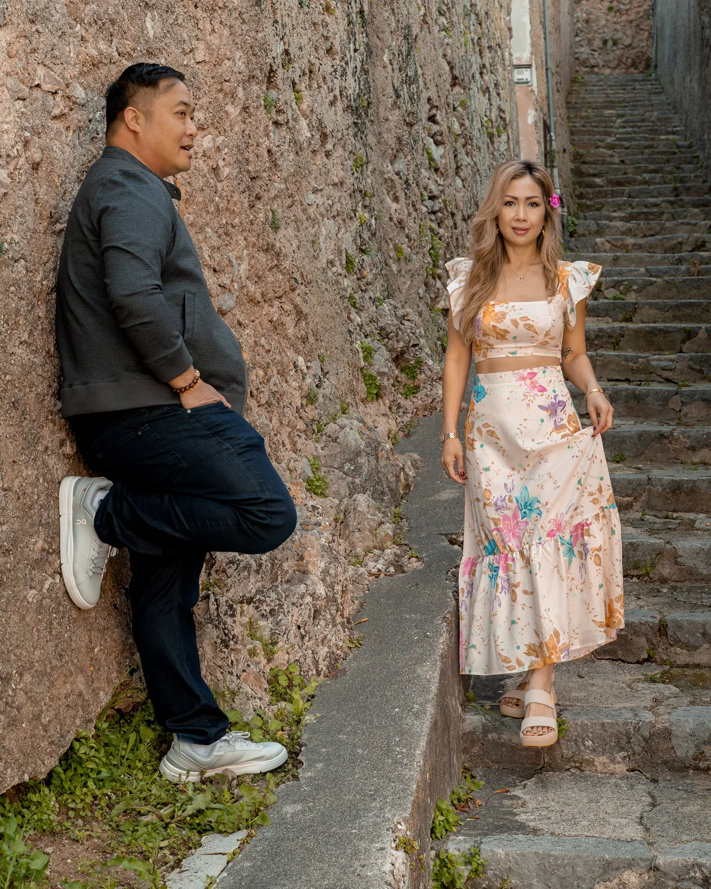 The couple standing apart beside a stone wall and staircase
