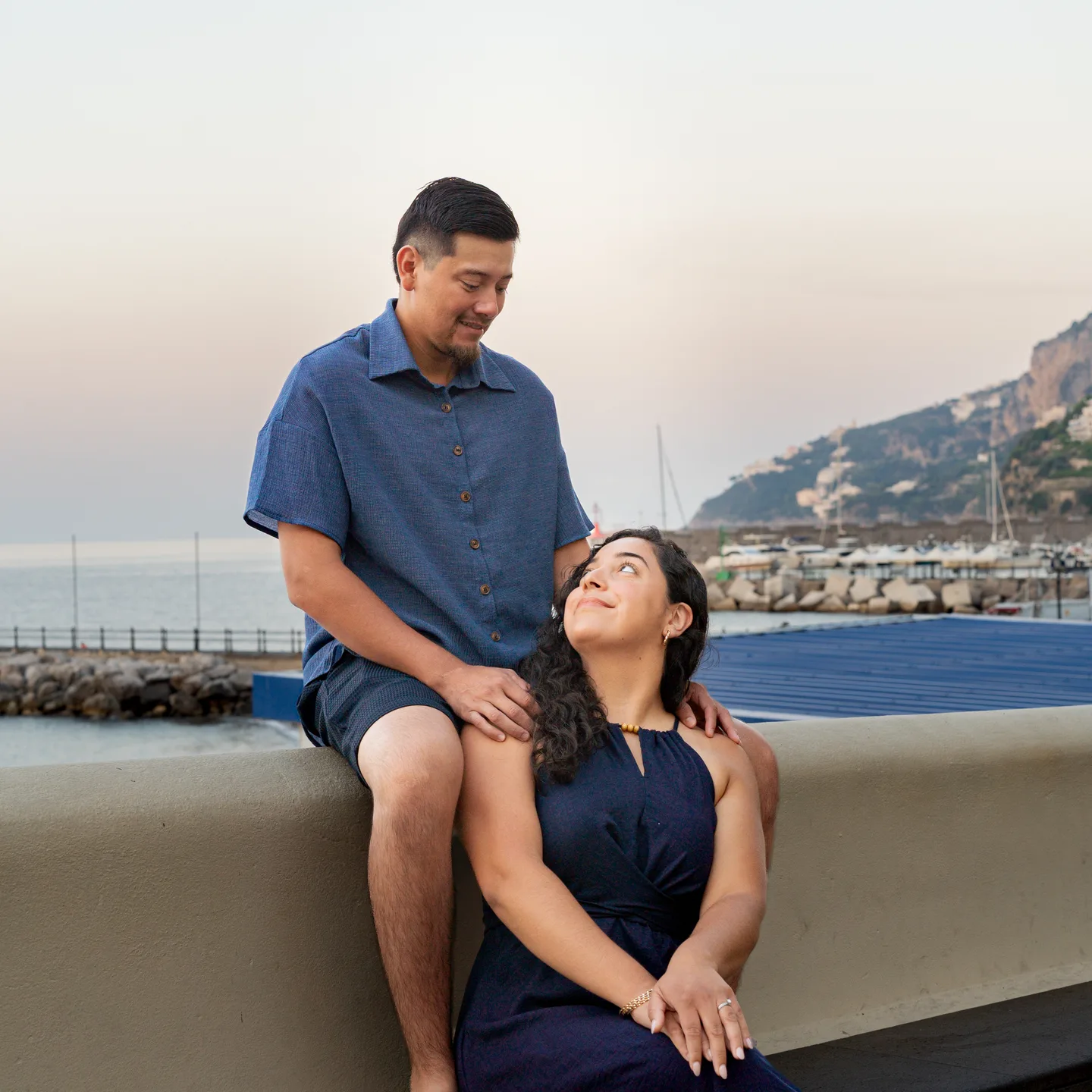 The couple seated at different heights beside Amalfi harbour