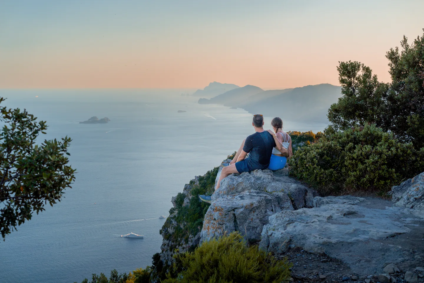 The couple on a rock above the coast at sunset
