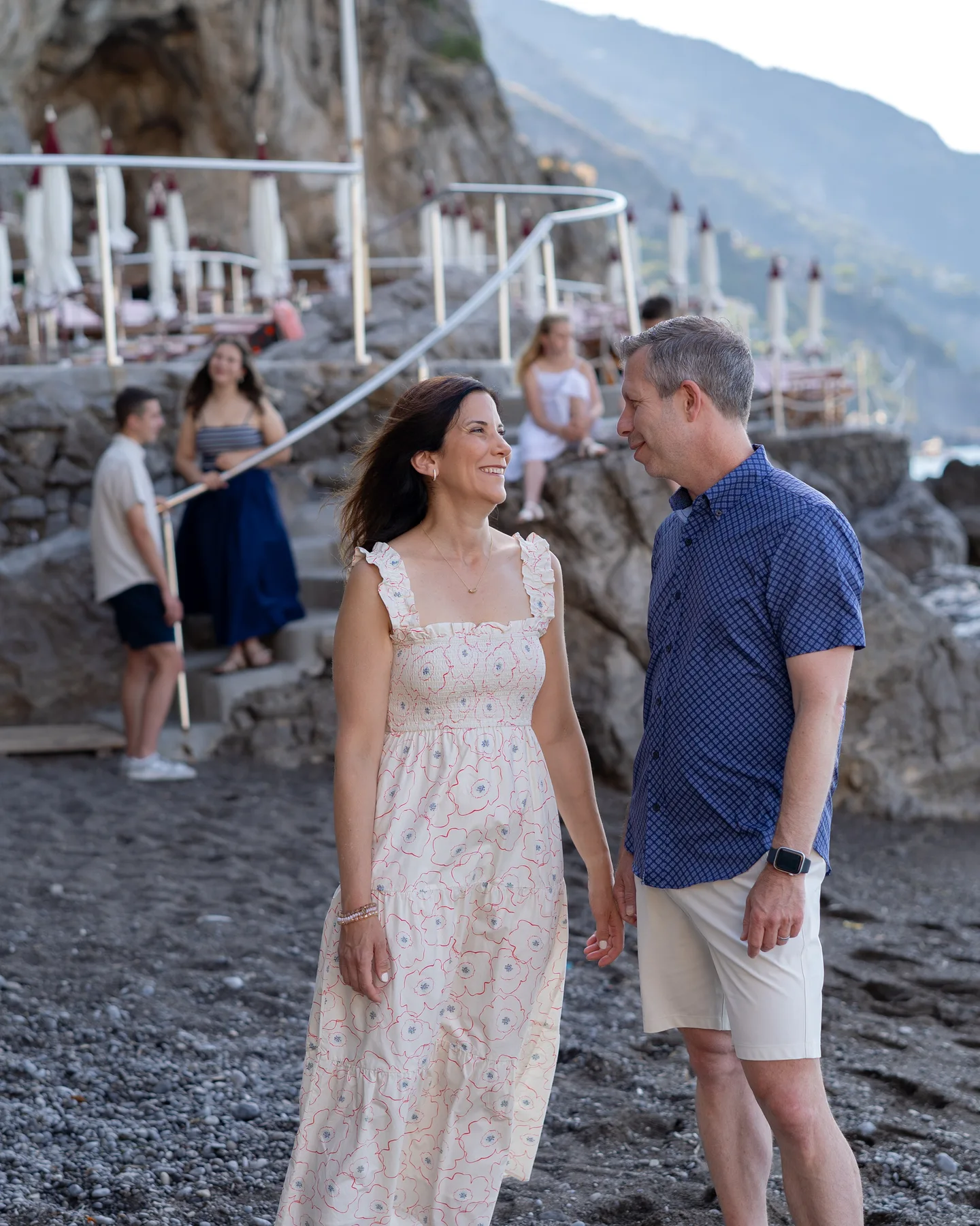 The couple smiling by the water with the children behind