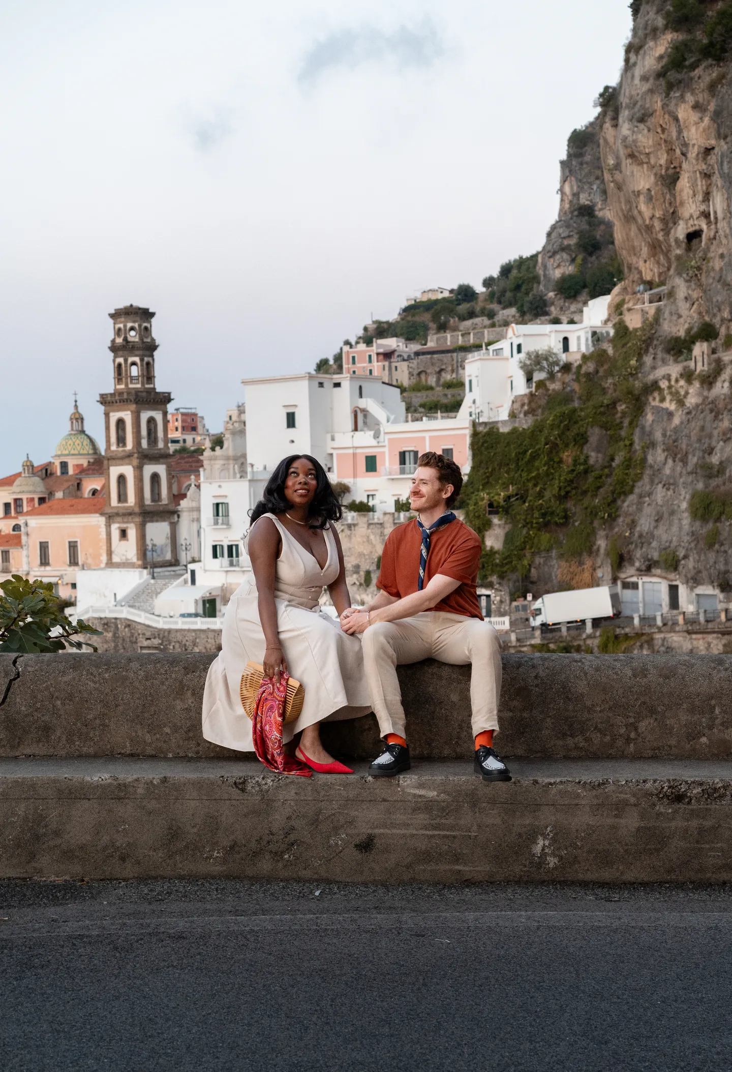 The couple seated on the sea wall with Atrani behind them